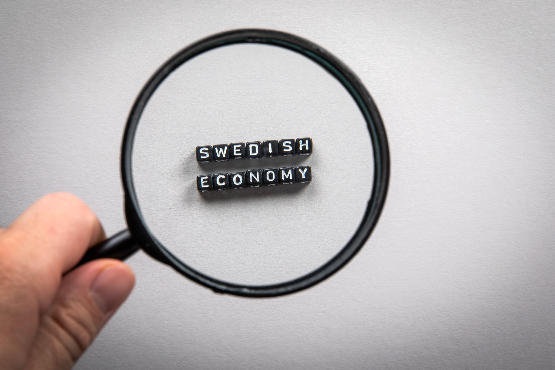 Economia Sueca. Mão do homem, segurando lupa. Importações e Exportações, Crescimento, Planejamento e Relatórios